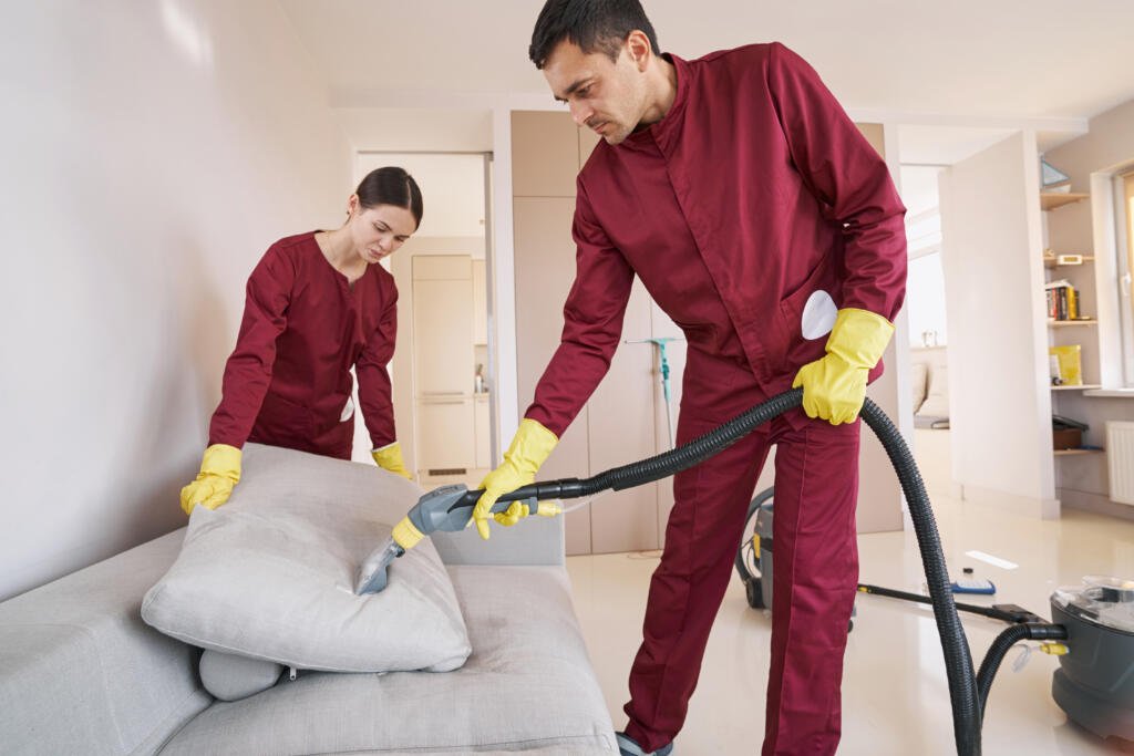 two skilled uniformed workers steam cleaning couch cushion